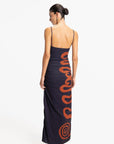 Woman wearing a long dress with orange patterns on a white background, back view