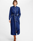 A model wearing a long-sleeved navy blue shirt dress with white contrast stitching and a matching tie belt, paired with brown leather boots, shot against a plain white studio background.
