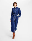 A model wearing a dark blue long-sleeve shirt dress with white contrast stitching and a matching tie belt, paired with brown leather boots, against a plain white studio background.