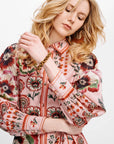 A woman wearing a pink long-sleeve button-up shirt with a bold red, green, and black floral print, photographed against a clean white background.