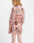 A woman shown from the back wearing a pink long-sleeve mini coat with a colorful floral and geometric pattern, paired with brown boots, against a plain white background.