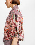 A side-profile view of a model wearing a short-sleeved blouse with a pink floral print and a red-and-white gingham collar, paired with a matching gingham skirt against a plain white background.