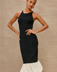Woman wearing a black dress with a white ruffled hem against a beige background front view