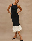 Woman wearing a black dress with a white ruffled hem against a beige background
