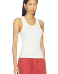 A woman modeling a white ribbed tank top paired with rust red drawstring pants against a plain white background.