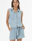 Woman wearing a light blue denim sleeveless shirt and shorts set on a white background