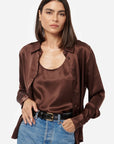 Woman wearing a brown satin shirt over a beige top with blue jeans on a white background