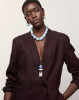 A model wearing a dark brown blazer, Sea and Sky Collar and Museo Cord II Necklace in Sea, posed against a solid off-white background.