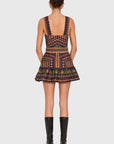 A model shown from the back wearing a sleeveless mini dress with a geometric pattern in navy, orange, and green, paired with black knee-high boots, against a light gray background.