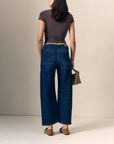 model waring blue jeans with a short sleeve brown top holding a woven bag on a cream background, back view