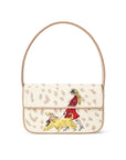 A beige textured shoulder bag with a tan leather handle, featuring a printed beige leopard print pattern and a colorful illustration of a woman in a red dress riding a yellow dog on the front flap.