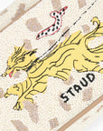 Close-up of a textured cream beaded fabric featuring a yellow embroidered dragon, a red-and-black spotted snake, and the word 'STAUD' in black beads.