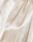 A close-up of draped cream satin fabric with a subtle dotted pattern of small metallic studs.