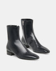 A pair of black leather ankle boots with pointed toes, low block heels, and side zippers, photographed on a clean light gray background.