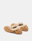A pair of tan suede slip-on slippers with fluffy cream shearling lining, shown from a side angle on a light gray background.