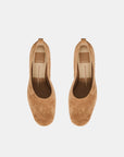 A pair of tan suede slip-on shoes with low block heels, shown from a top-down view on a light gray background.