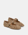 A pair of taupe suede Mary Jane flats decorated with gold-tone metal studs and buckles, shown against a light gray background.