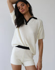 Woman wearing a white outfit with black accents against a plain background