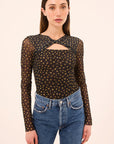 Woman wearing a black sheer top with gold polka dots and blue jeans on a beige background