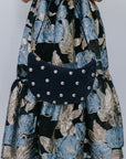 Person wearing a floral dress holding a navy studded handbag against a plain background