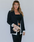 Woman in a black blazer holding a gold clutch against a plain background