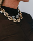 Close-up of a person wearing a gold and silver chain necklace against a neutral background