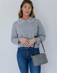 model wearing grey crochet collar cardigan with jeans and a black and white checker bag on a white background