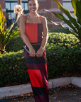 Woman in a colorful dress standing outdoors with plants and a building in the background
