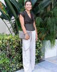 Woman in a brown top and beige pants standing in front of green plants