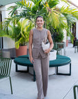 Woman in a beige outfit standing on a patio with plants and furniture.