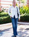 Woman in a white shirt and blue jeans standing outdoors with greenery in the background
