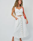 Woman wearing a white sleeveless top and white skirt with gold buttons on a plain background