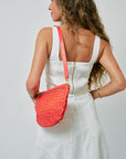 Woman wearing a white dress with a red woven leather handbag on a plain background