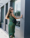 Woman in a green dress standing next to a building with large windows with black perforated grande fanny on shoulder
