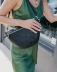 Woman in green outfit holding a black perforated grande fanny with a blurred background