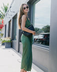 Woman in a green dress standing outside a building with large windows with black perforated grande fanny