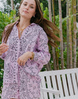 Woman wearing a pink paisley outfit standing outdoors with greenery in the background