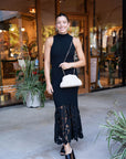 Woman in a black dress with lace details standing outside a store.
