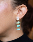 Close-up of an ear wearing a pearl and turquoise stone earring.