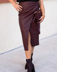 Woman wearing a black top and maroon skirt standing against a white wall.