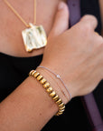 Close-up of a person's wrist wearing gold bracelets with a blurred background
