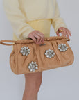 Person holding a beige handbag with decorative flowers against a white background
