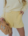 Person wearing a yellow outfit with a beige clutch against a white background