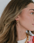 Close-up of a person wearing gold hoop earrings and a gold chain necklace.