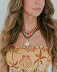 Woman wearing a top with shell designs and multiple necklaces against a white background