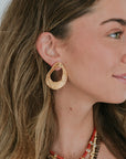 Close-up of a woman wearing gold hoop earrings and multiple necklaces.