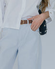 Person wearing a white shirt, light blue pants, and a brown belt with a blurred background, close up denim front