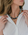 Woman wearing a white shirt with a necklace featuring blue and gold elements.