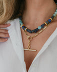 Necklace with blue and gold beads worn by a person against a white shirt background