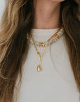 Close-up of a person wearing a gold necklace with a heart pendant and another necklace with beads.
